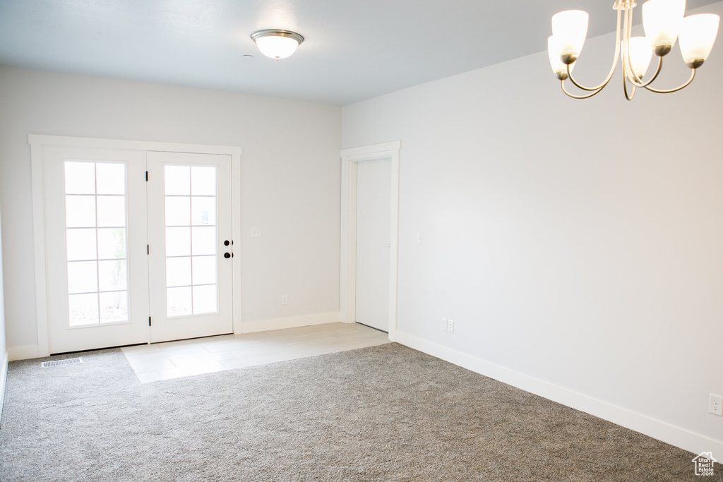 Empty room featuring plenty of natural light, a notable chandelier, and light colored carpet