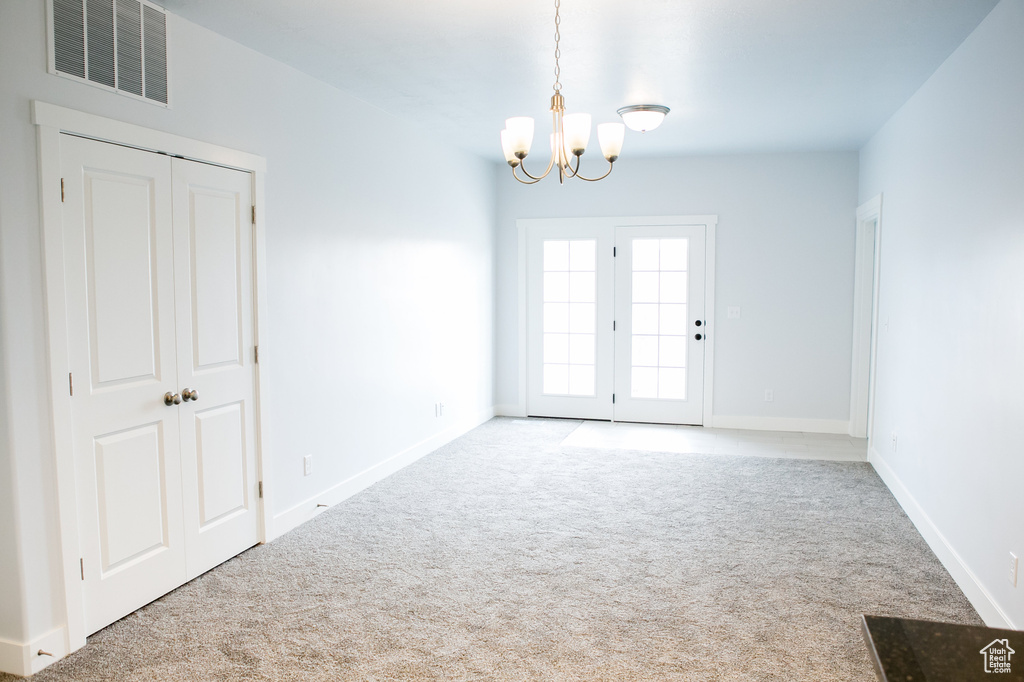 Unfurnished room featuring an inviting chandelier and light carpet