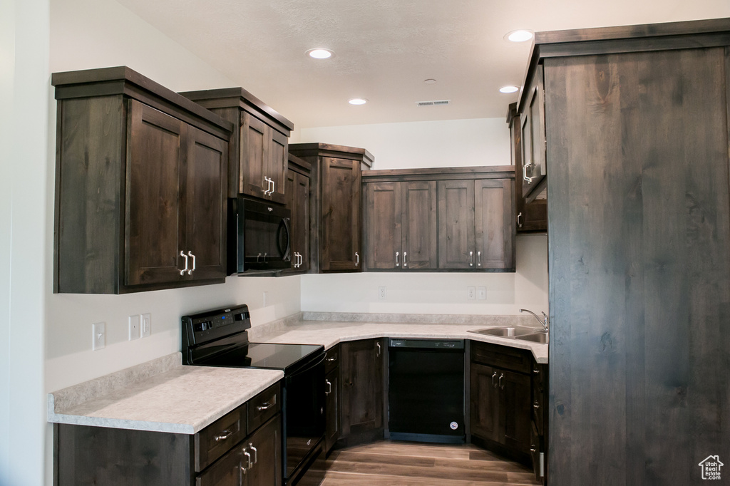 Kitchen with dark brown cabinets, sink, black appliances, and light hardwood / wood-style floors