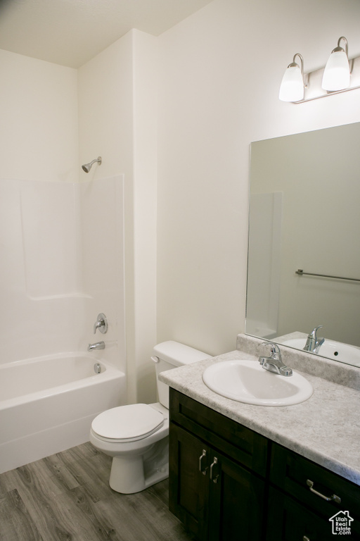 Full bathroom with vanity with extensive cabinet space, hardwood / wood-style floors, toilet, and shower / tub combination