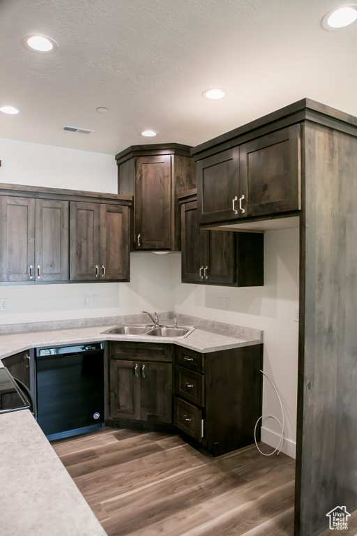 Kitchen with dark brown cabinets, sink, black dishwasher, and hardwood / wood-style flooring
