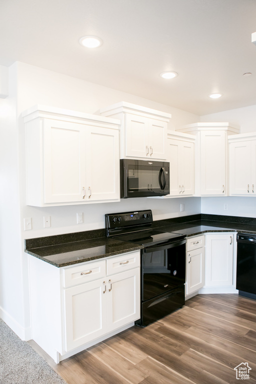 Kitchen featuring white cabinets, dark stone counters, black appliances, and light hardwood / wood-style floors