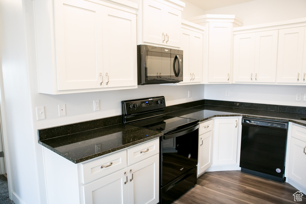 Kitchen with black appliances, dark stone countertops, dark wood-type flooring, and white cabinetry