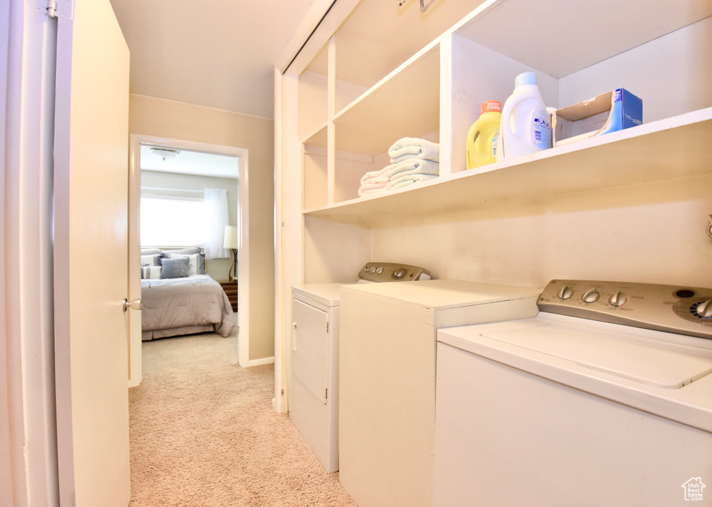 Clothes washing area featuring washer and clothes dryer and light colored carpet