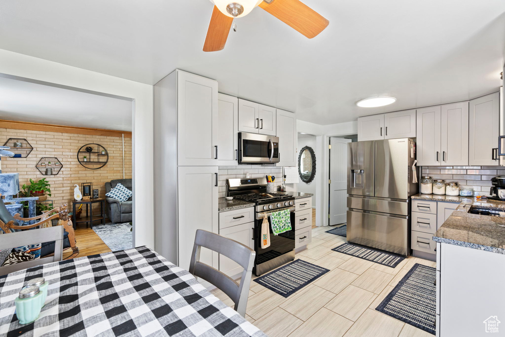 Kitchen with ceiling fan, stainless steel appliances, backsplash, and white cabinetry