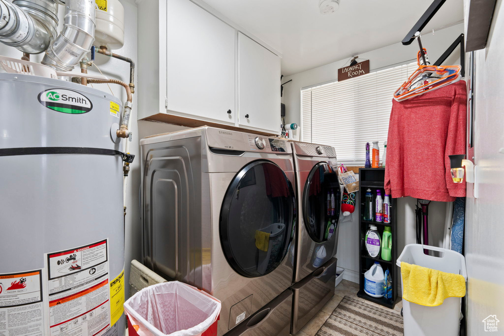 Clothes washing area featuring water heater, washer and dryer, and cabinets