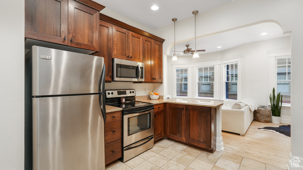 Kitchen featuring appliances with stainless steel finishes, light stone counters, pendant lighting, and light tile floors