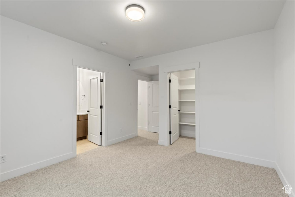 Unfurnished bedroom with a spacious closet, light carpet, a closet, and connected bathroom