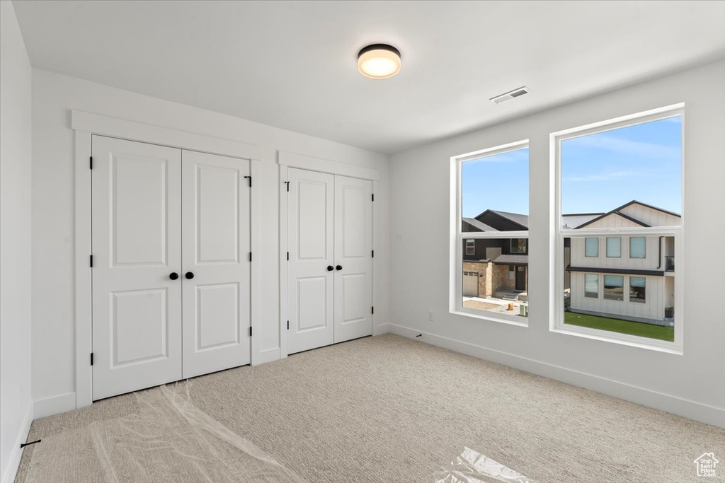 Unfurnished bedroom with light colored carpet and two closets