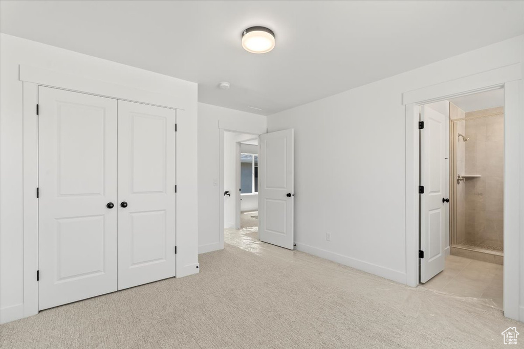 Unfurnished bedroom featuring light colored carpet, a closet, and ensuite bath