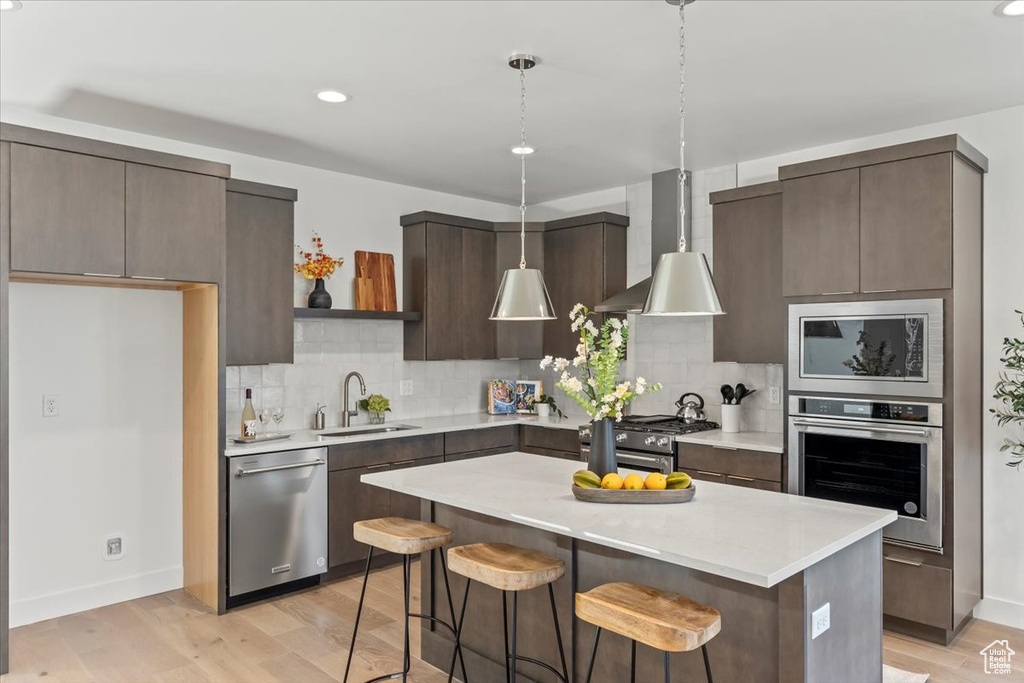 Kitchen with light hardwood / wood-style flooring, backsplash, wall chimney exhaust hood, appliances with stainless steel finishes, and sink