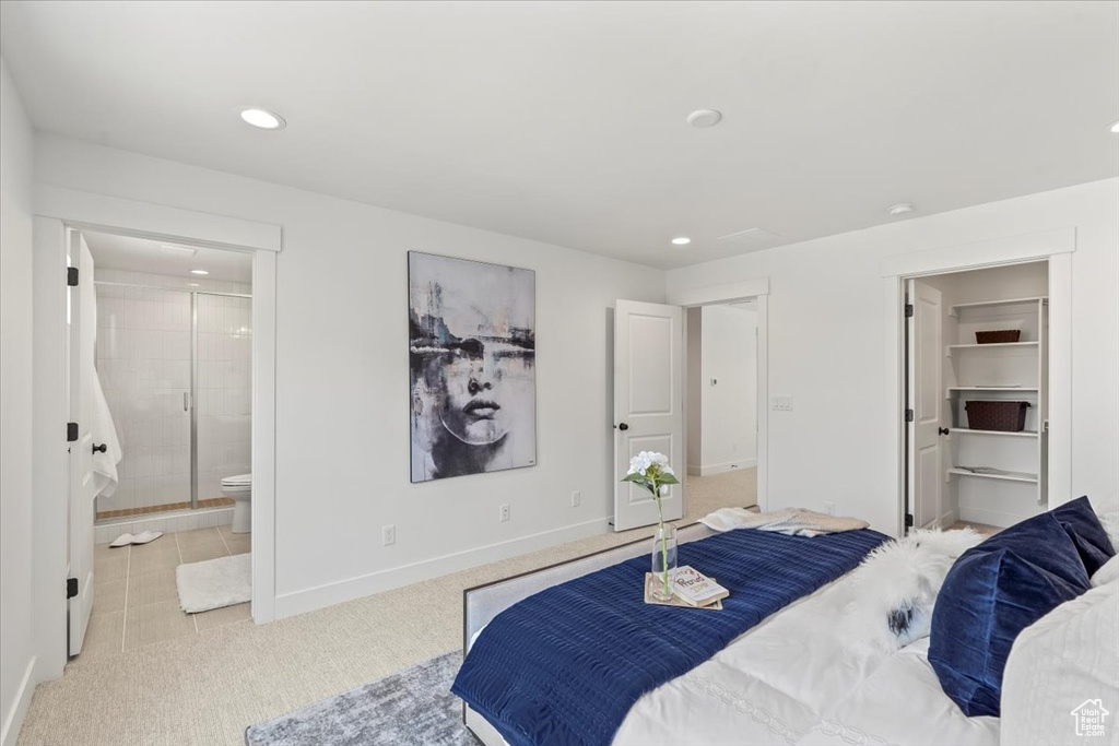 Bedroom with ensuite bathroom, a walk in closet, and light colored carpet