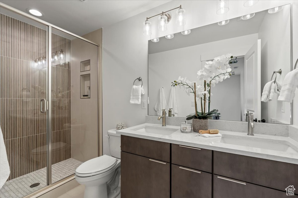 Bathroom featuring a shower with door, toilet, and dual bowl vanity