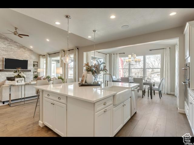 Kitchen with pendant lighting, white cabinets, vaulted ceiling, and light hardwood / wood-style flooring