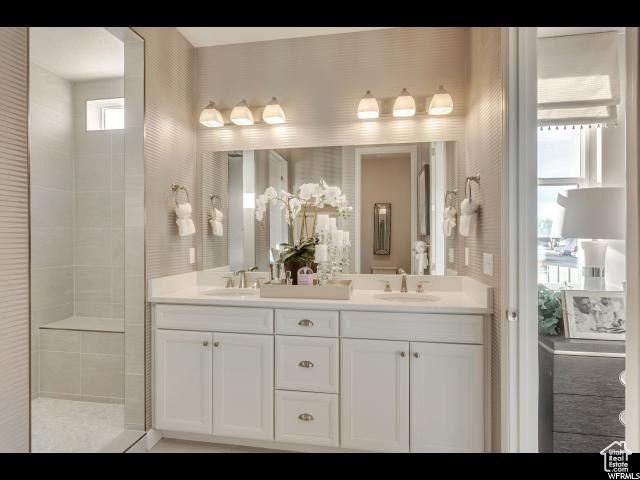 Bathroom with dual sinks, a tile shower, a wealth of natural light, and oversized vanity
