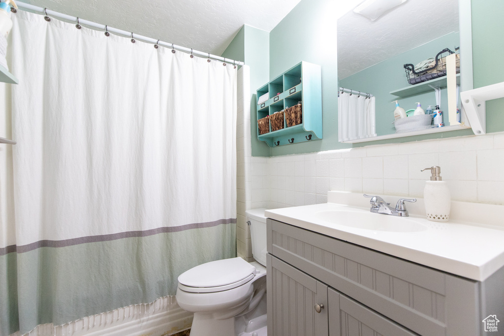 Bathroom featuring tasteful backsplash, tile walls, oversized vanity, and toilet