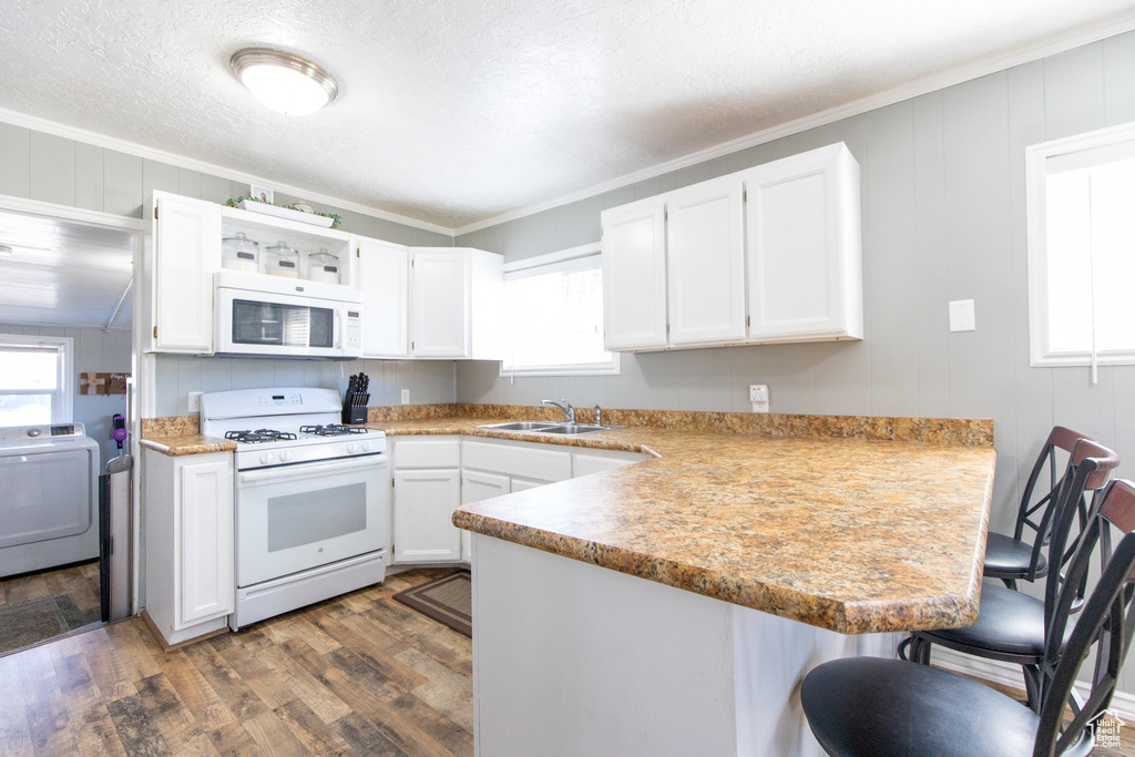Kitchen with dark hardwood / wood-style floors, washer / dryer, kitchen peninsula, a breakfast bar area, and white appliances
