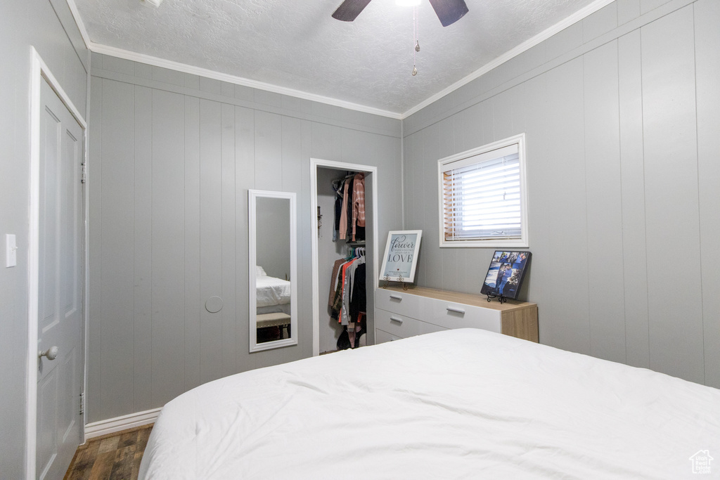 Bedroom with a closet, ceiling fan, crown molding, and dark wood-type flooring