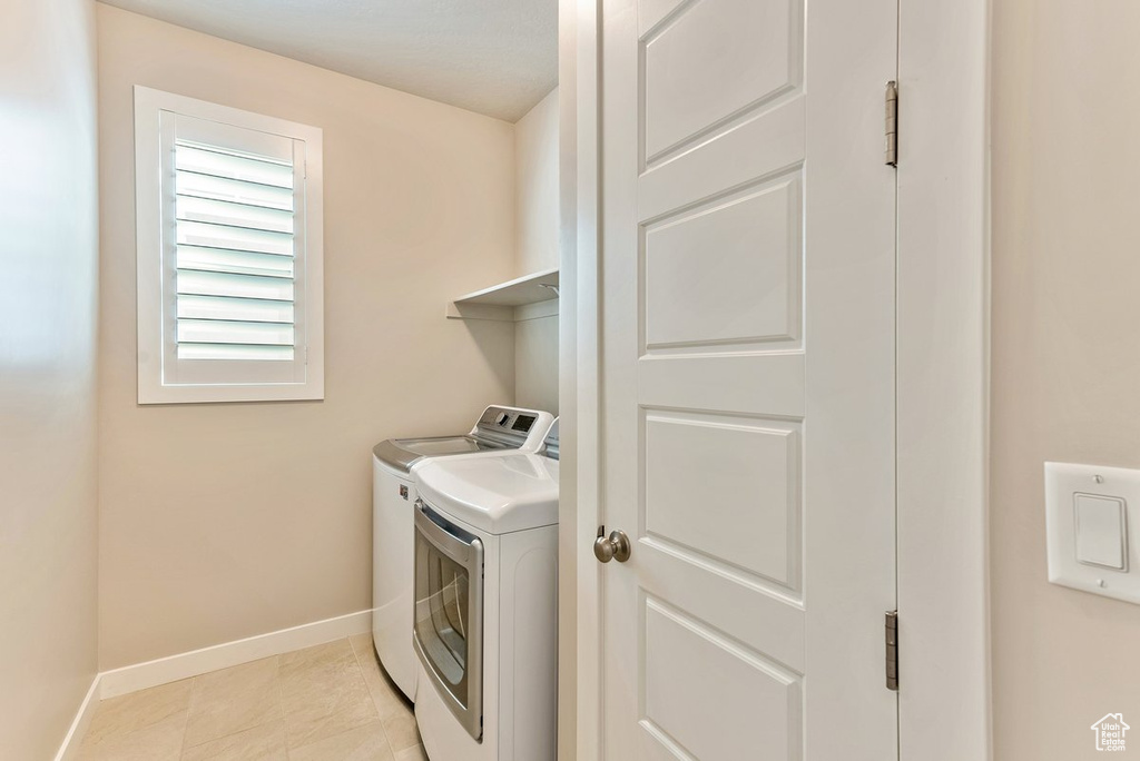 Clothes washing area with light tile floors and separate washer and dryer