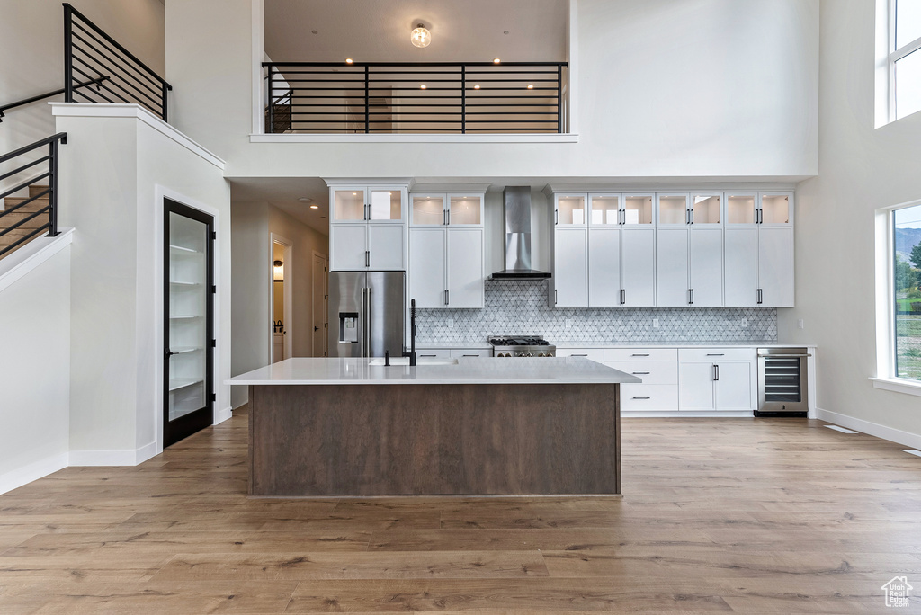 Kitchen featuring beverage cooler, high quality fridge, wall chimney exhaust hood, a high ceiling, and light hardwood / wood-style floors