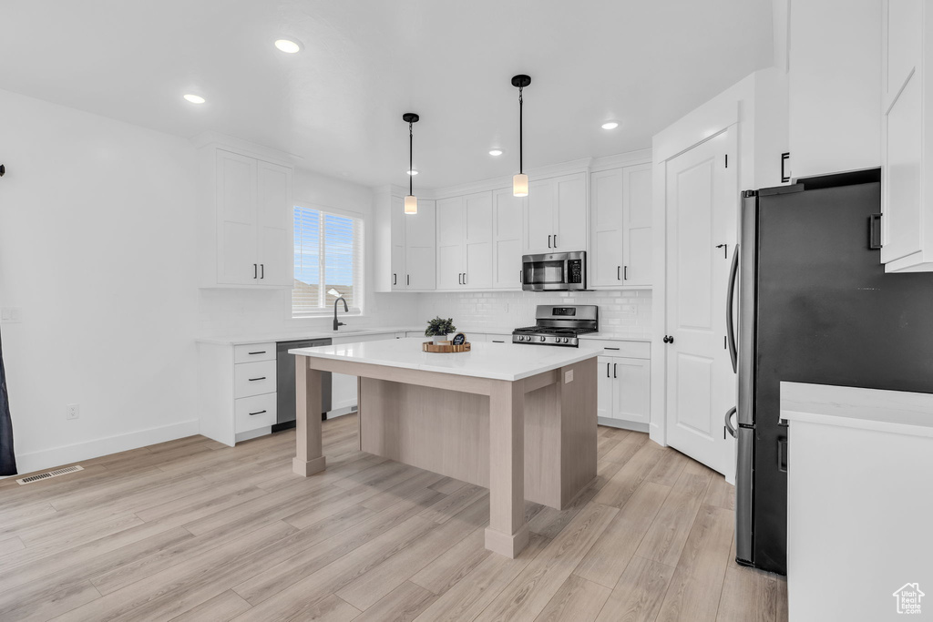 Kitchen featuring appliances with stainless steel finishes, white cabinetry, pendant lighting, and a center island