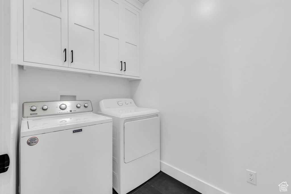 Laundry area featuring cabinets, dark tile flooring, and separate washer and dryer