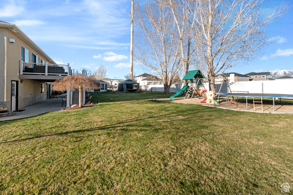 View of yard featuring a patio area, a balcony, a trampoline, and a playground