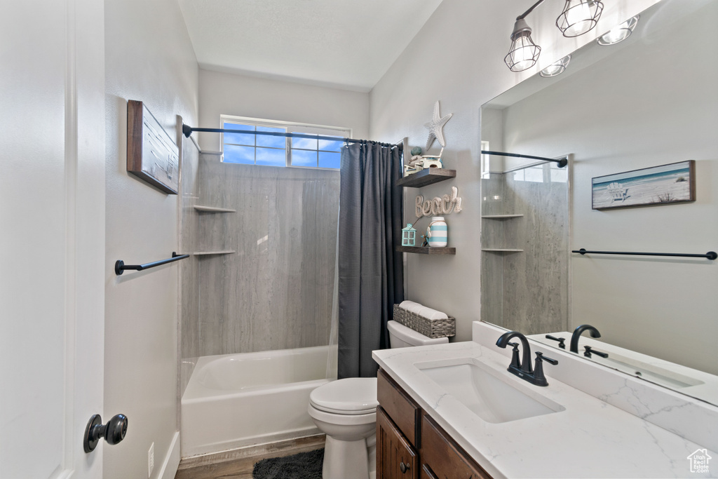 Full bathroom featuring hardwood / wood-style floors, toilet, vanity with extensive cabinet space, and shower / bath combination with curtain