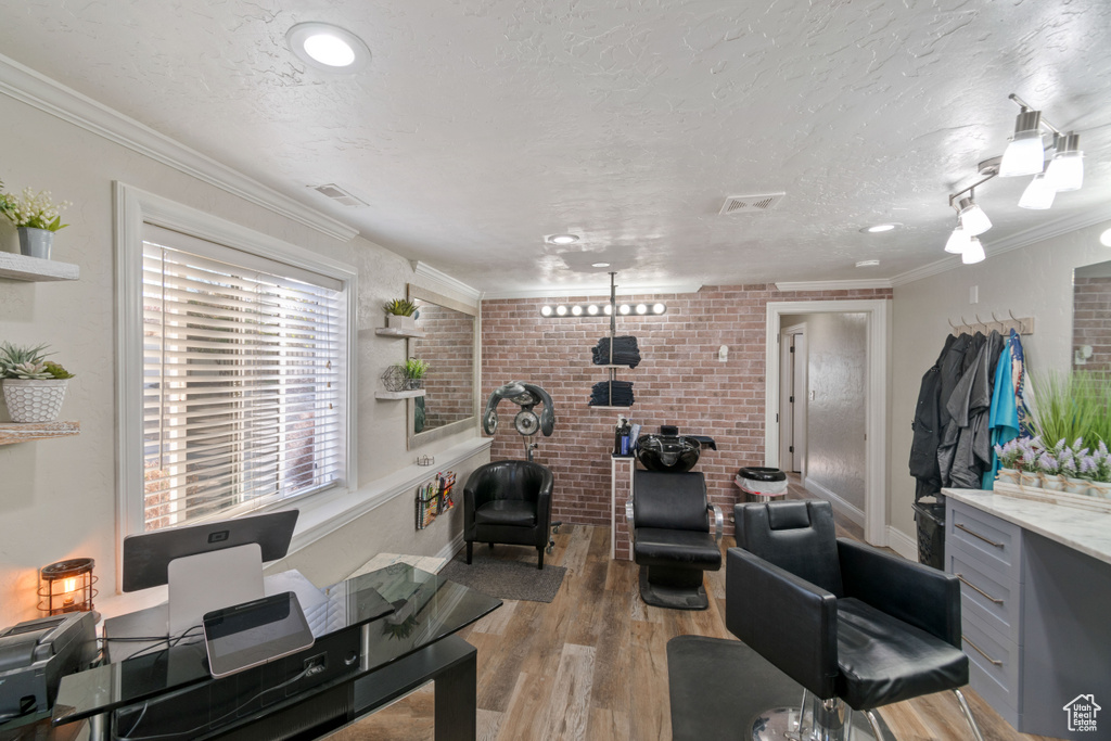 Home office featuring light wood-type flooring, ornamental molding, a textured ceiling, and brick wall