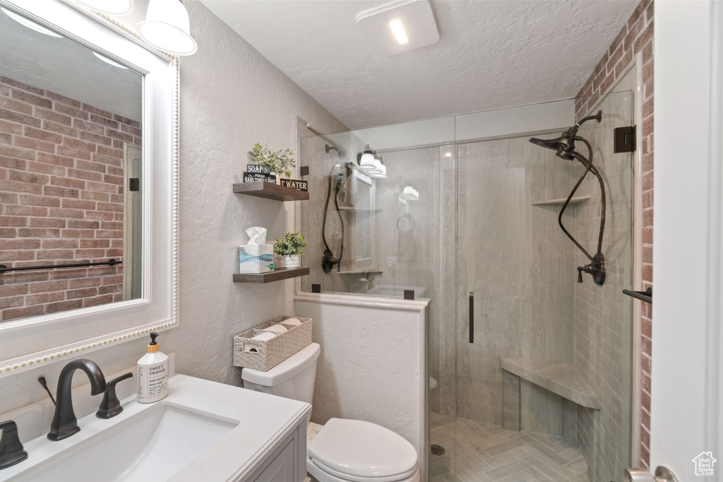 Bathroom with a shower with door, vanity, toilet, and a textured ceiling