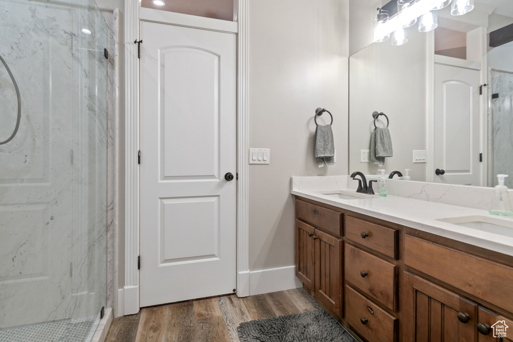Bathroom with wood-type flooring, a shower with shower door, double sink, and oversized vanity