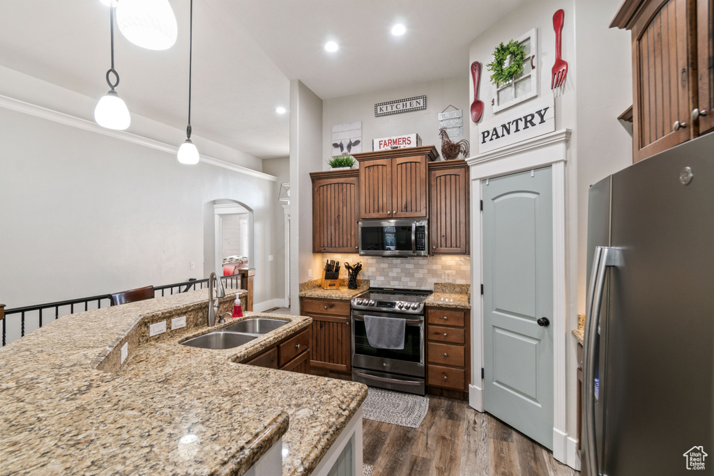 Kitchen featuring pendant lighting, sink, light stone countertops, stainless steel appliances, and dark wood-type flooring