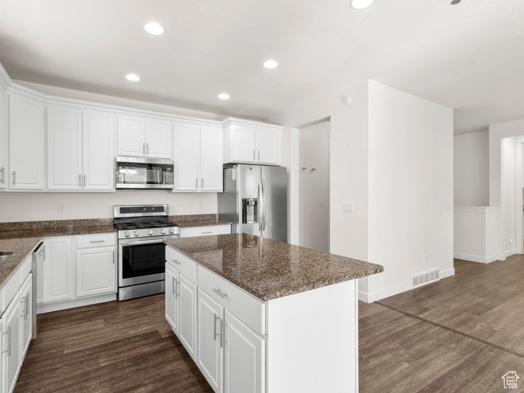 Kitchen with appliances with stainless steel finishes, white cabinetry, dark wood-type flooring, and a center island