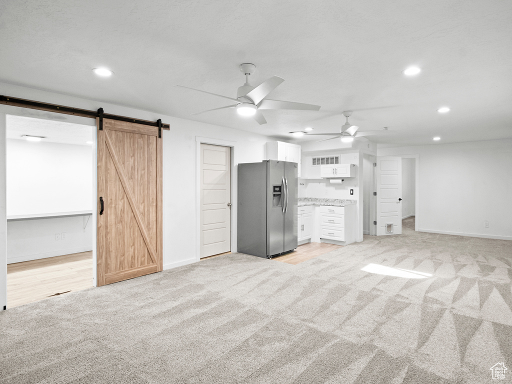 Basement with light colored carpet, a barn door, ceiling fan, and stainless steel fridge