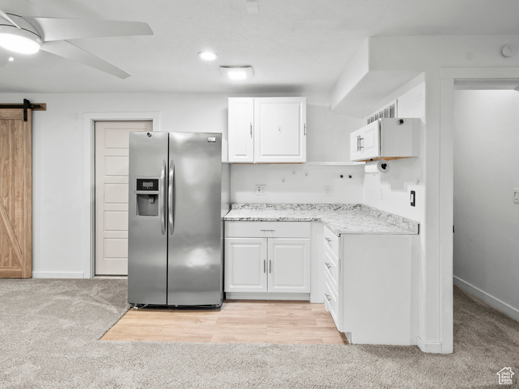 Kitchen featuring a barn door, stainless steel refrigerator with ice dispenser, light colored carpet, ceiling fan, and white cabinetry