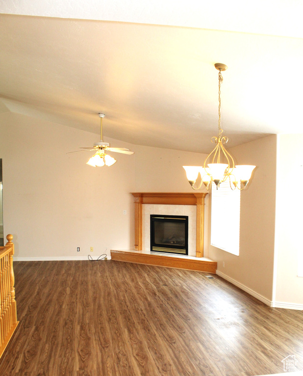 Unfurnished living room featuring hardwood / wood-style floors, vaulted ceiling, a tiled fireplace, and ceiling fan with notable chandelier