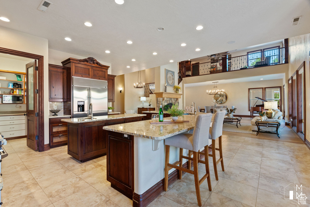 Kitchen with a kitchen island with sink, built in appliances, a breakfast bar, light stone countertops, and a chandelier