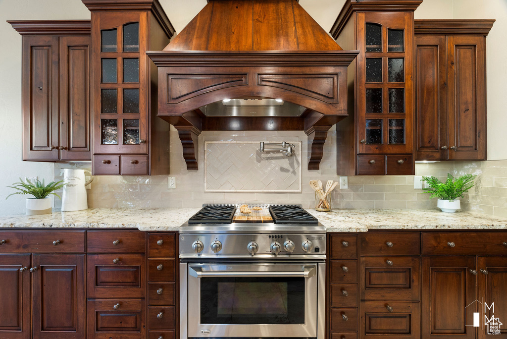 Kitchen with light stone countertops, tasteful backsplash, stainless steel range, and premium range hood