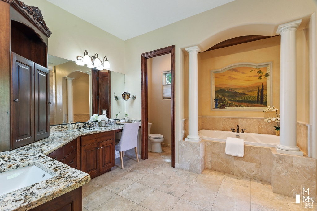 Bathroom with ornate columns, vanity, tile flooring, and tiled tub