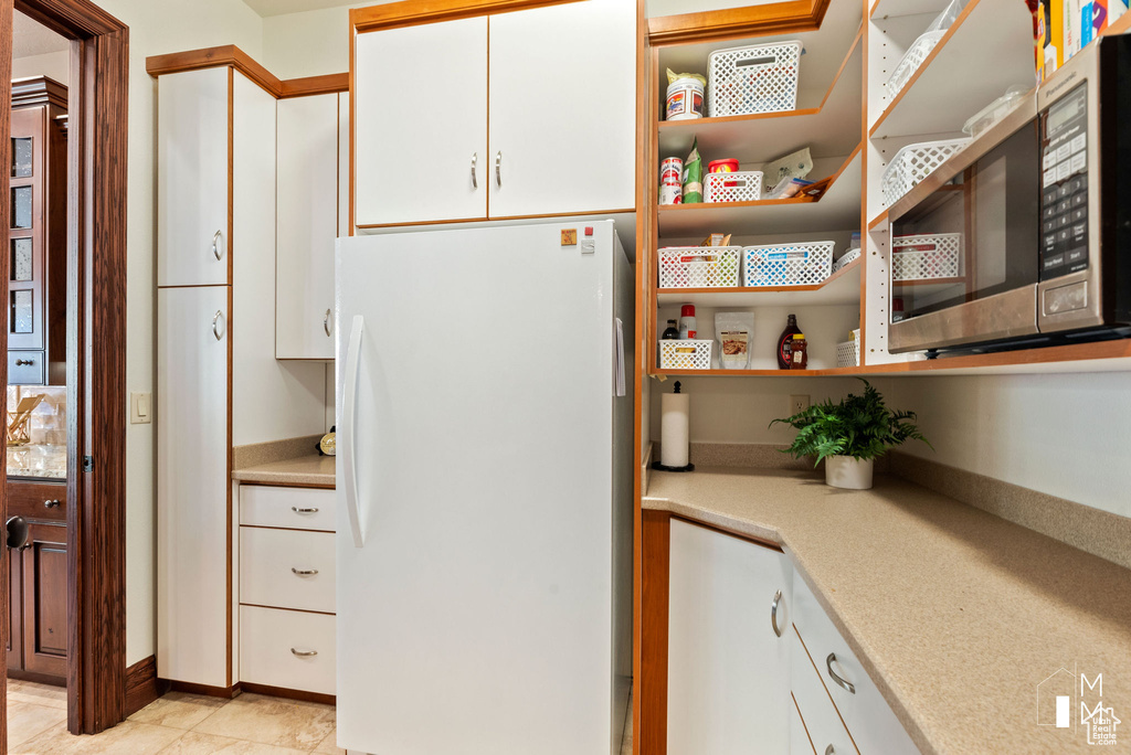 Kitchen with white fridge, white cabinetry, and light tile floors