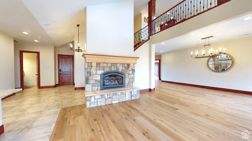 Unfurnished living room with an inviting chandelier, a stone fireplace, and light hardwood / wood-style floors