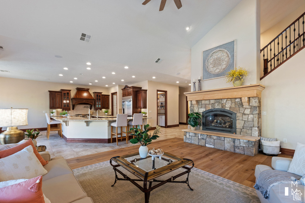 Living room featuring a stone fireplace, light hardwood / wood-style floors, high vaulted ceiling, and ceiling fan