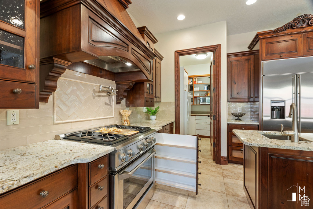 Kitchen featuring backsplash, light stone counters, premium appliances, light tile floors, and sink