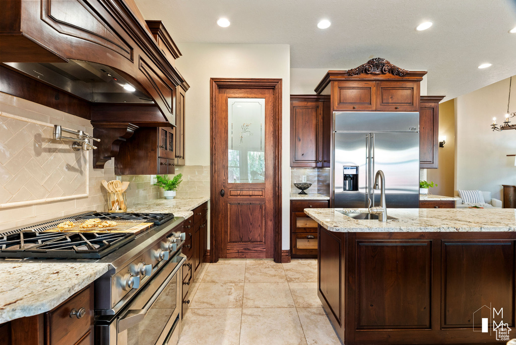 Kitchen featuring premium range hood, high end appliances, light stone countertops, and tasteful backsplash
