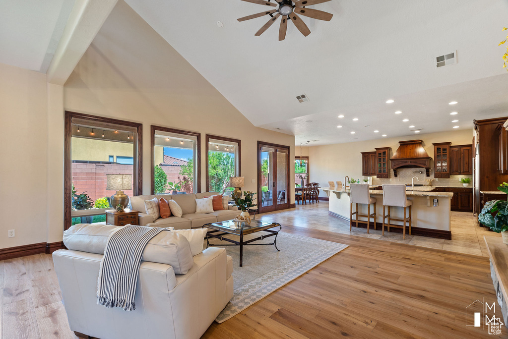 Living room featuring ceiling fan, french doors, light hardwood / wood-style flooring, sink, and high vaulted ceiling