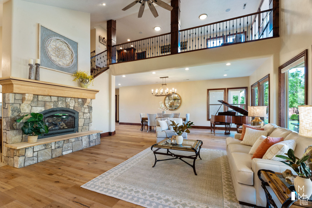 Living room featuring a stone fireplace, a towering ceiling, ceiling fan with notable chandelier, and light hardwood / wood-style floors