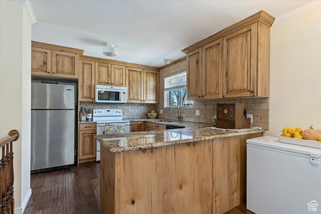Kitchen featuring white appliances, backsplash, dark hardwood / wood-style flooring, kitchen peninsula, and stone counters