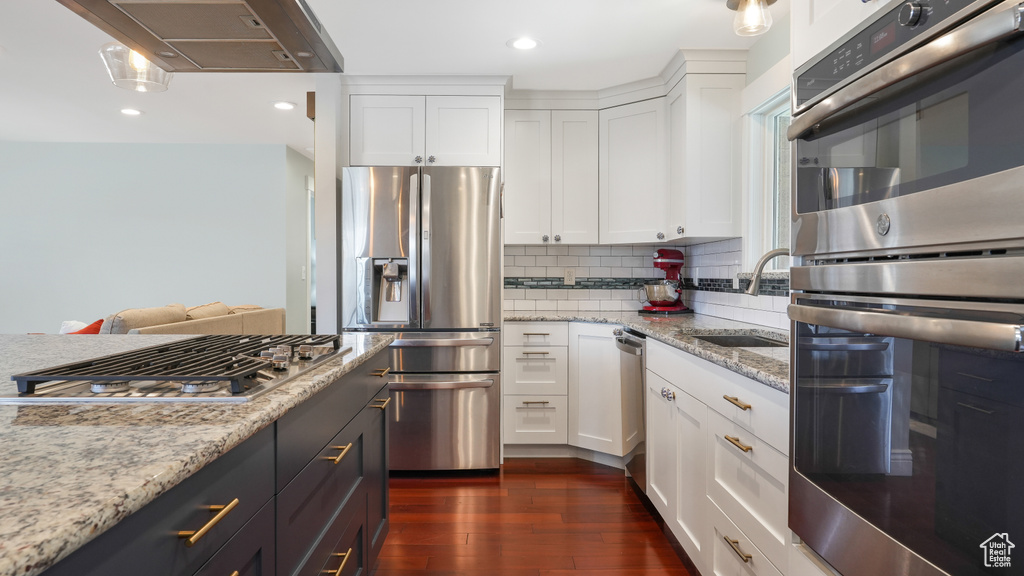 Kitchen with appliances with stainless steel finishes, white cabinets, light stone counters, dark wood-type flooring, and tasteful backsplash