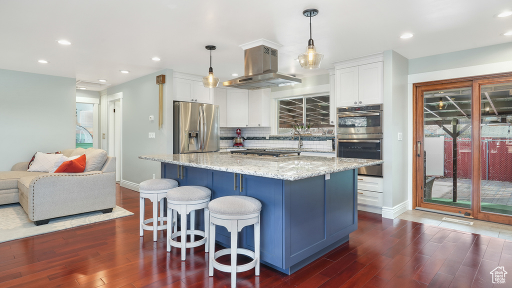 Kitchen featuring white cabinetry, hanging light fixtures, appliances with stainless steel finishes, and island exhaust hood
