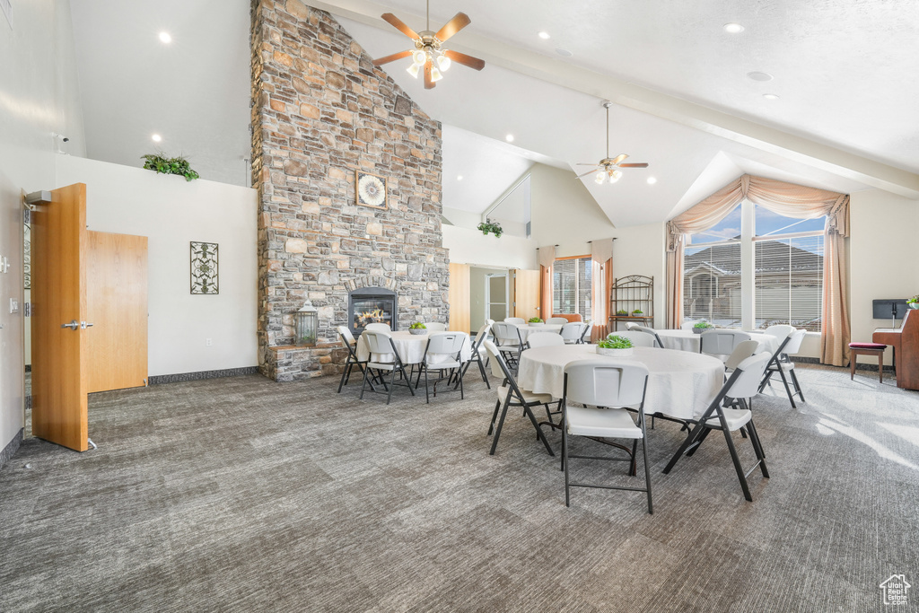 Carpeted dining area featuring a fireplace, ceiling fan, high vaulted ceiling, and beamed ceiling